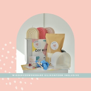 May include: A candle making DIY kit featuring a white box labeled DIY KIT, a tan pouch, a translucent silicone arch mold, blue gloves, wooden stir sticks, and three finished arch-shaped candles in cream, pink, and light pink colors.