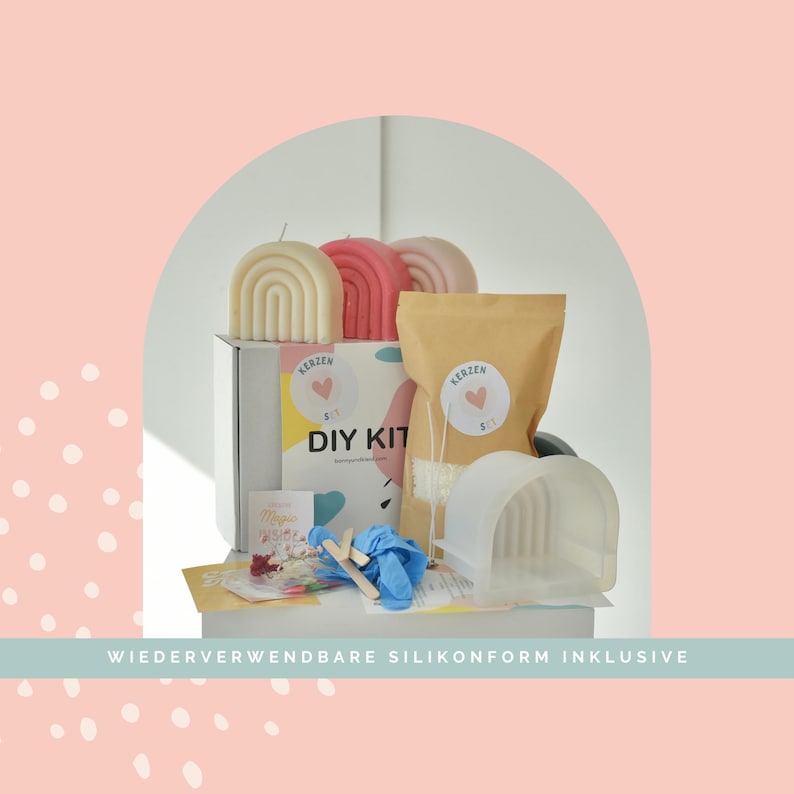 May include: A candle making DIY kit featuring a white box labeled DIY KIT, a tan pouch, a translucent silicone arch mold, blue gloves, wooden stir sticks, and three finished arch-shaped candles in cream, pink, and light pink colors.