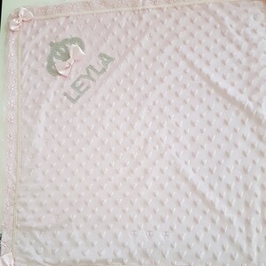 May include: A pink baby blanket with a white lace border and a silver crown and the name "LEYLA" embroidered on it.