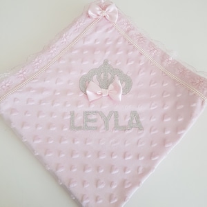 May include: Pink baby blanket with a crown and the name "LEYLA" embroidered in silver rhinestones.
