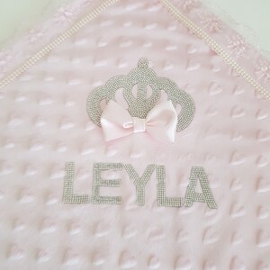 May include: Pink baby blanket with a crown and the name "LEYLA" embroidered in silver rhinestones.