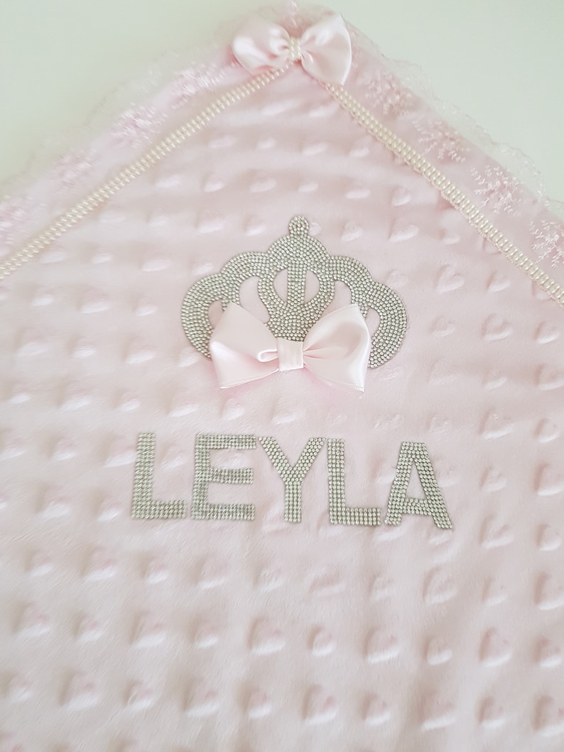 May include: Pink baby blanket with a crown and the name "LEYLA" embroidered in silver rhinestones.