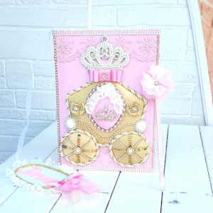 May include: Pink and gold carriage party favor box with a white lace trim, a gold crown, and a pink flower. The box is decorated with gold glitter and rhinestones.