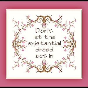 May include: A white cross-stitch embroidery with a brown floral border and the text "Don't let the existential dread set in".