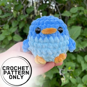 May include: A crocheted blue bird plush toy with a light blue and white pattern. The bird has black eyes, an orange beak, and orange feet.