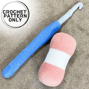 May include: A crochet hook and a pink and white striped crocheted cushion. The crochet hook is blue and white. The cushion is a cylindrical shape.
