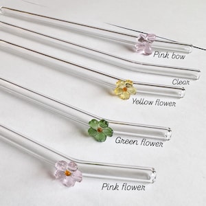 May include: Clear glass straws with decorative flower accents in pink, yellow, and green. The straws have a slight bend at the top and are labeled with the text "Pink bow", "Clear", "Yellow flower", "Green flower", and "Pink flower".