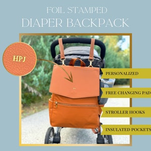 May include: A foil stamped diaper backpack in a warm orange hue, featuring a flap closure and multiple pockets. The bag includes stroller hooks and insulated pockets. The text "FOIL STAMPED DIAPER BACKPACK" is at the top. The bag is personalized with the initials "HPJ".