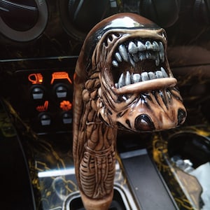 Könnte beinhalten: Ein brauner und schwarzer, alienförmiger Schaltknauf mit einem zahnigen Mund und einer detaillierten, strukturierten Oberfläche.