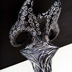 Pu&ograve; includere: Scultura in ceramica nera e bianca con una base a forma di stella e due corna curve con intricati disegni bianchi.