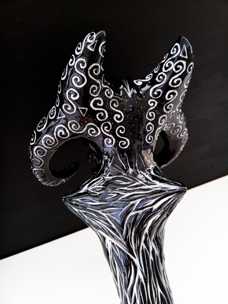 Pu&ograve; includere: Scultura in ceramica nera e bianca con una base a forma di stella e due corna curve con intricati disegni bianchi.