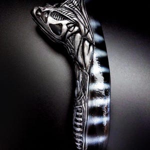 May include: A silver and black alien head sculpture with a detailed design. The sculpture is made of a smooth, hard material and has a glossy finish.