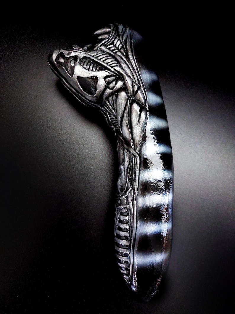 May include: A silver and black alien head sculpture with a detailed design. The sculpture is made of a smooth, hard material and has a glossy finish.