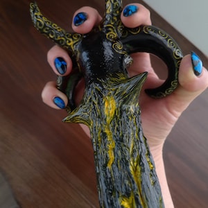 Pu&ograve; includere: Una spada decorativa nera e dorata con un design dettagliato. La spada ha una superficie testurizzata e una punta appuntita.
