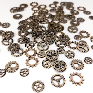 Op de afbeelding: Een verzameling antieke, goudkleurige metalen tandwielen van verschillende groottes. De tandwielen zijn verspreid over een wit oppervlak.
