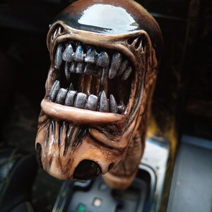 May include: A brown and black alien-shaped gear shift knob with a toothy, open mouth and a shiny black top.