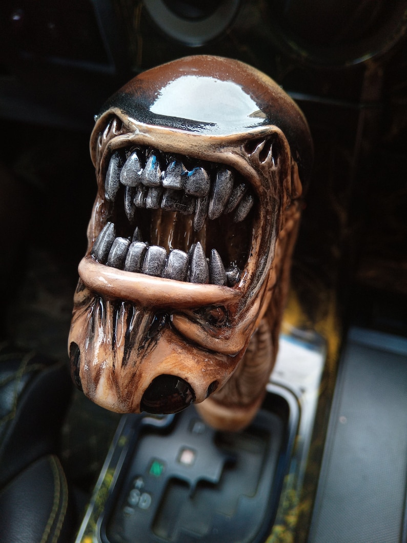 May include: A brown and black alien-shaped gear shift knob with a toothy, open mouth and a shiny black top.
