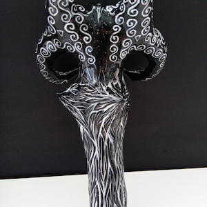 Pu&ograve; includere: Maschera in ceramica nera e bianca con intricati disegni a spirale. La maschera ha due corna e un viso lungo e stretto.