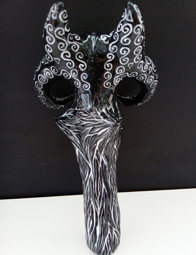 Pu&ograve; includere: Maschera in ceramica nera e bianca con intricati disegni a spirale. La maschera ha due corna e un viso lungo e stretto.