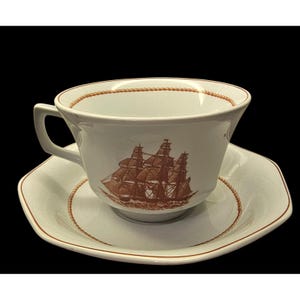 May include: White teacup and saucer set with a brown sailing ship design. The cup and saucer have a brown rope-like trim around the edges. The cup has a handle and the saucer is octagonal.