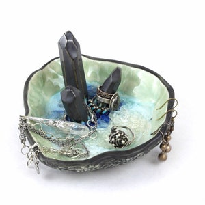May include: A ceramic ring dish with a blue and green glaze. The dish features three black crystal points and is filled with jewelry, including rings, earrings, and necklaces.