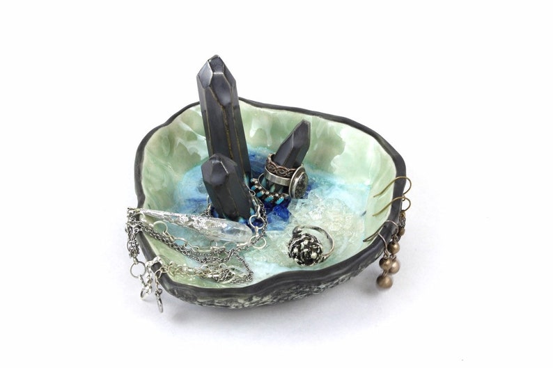 May include: A ceramic ring dish with a blue and green glaze. The dish features three black crystal points and is filled with jewelry, including rings, earrings, and necklaces.