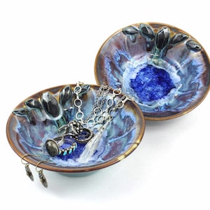 May include: Two ceramic bowls with a blue and brown glaze. The bowls are shaped like flowers and have a raised design. The bowls are filled with jewelry, including rings, earrings, and necklaces.
