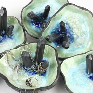 May include: Set of five ceramic ring dishes with a light green glaze and a blue and white glaze. Each dish features black crystal-shaped accents.