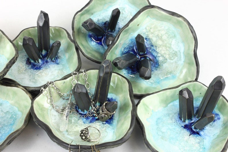 May include: Set of five ceramic ring dishes with a light green glaze and a blue and white glaze. Each dish features black crystal-shaped accents.