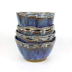 May include: A set of four ceramic bowls stacked on top of each other. The bowls are a deep blue color with brown and gold accents. The bowls have a unique, textured design.
