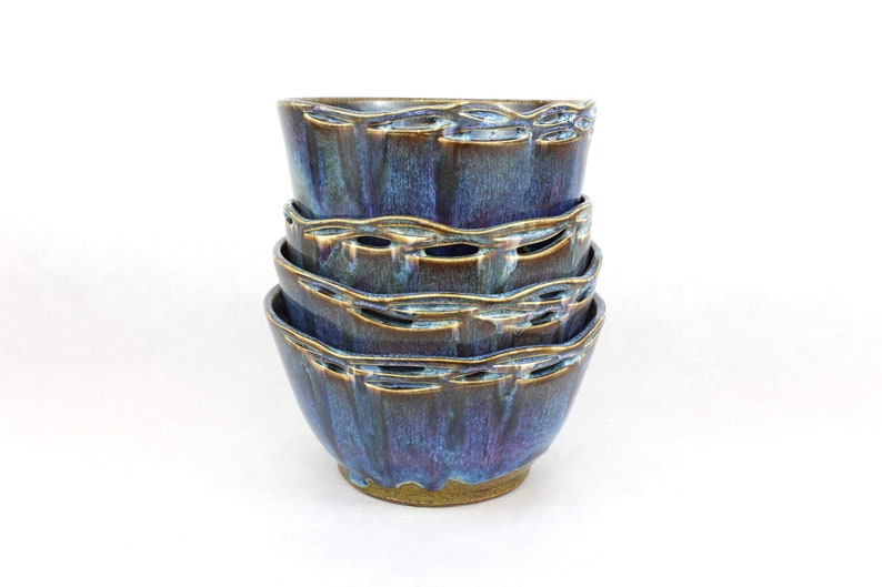 May include: A set of four ceramic bowls stacked on top of each other. The bowls are a deep blue color with brown and gold accents. The bowls have a unique, textured design.