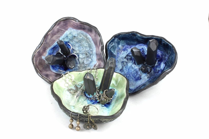 May include: Three ceramic ring dishes with a geode design. Each dish features black crystal accents and a different color glaze: purple, blue, and green.