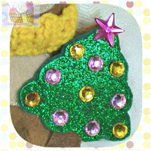 Puede incluir: Un &aacute;rbol de Navidad de fieltro verde con purpurina rosa y amarilla y pedrer&iacute;a. El &aacute;rbol tiene una estrella rosa en la parte superior.