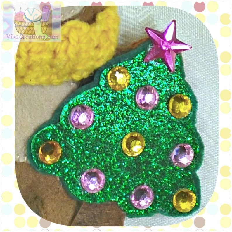 Puede incluir: Un &aacute;rbol de Navidad de fieltro verde con purpurina rosa y amarilla y pedrer&iacute;a. El &aacute;rbol tiene una estrella rosa en la parte superior.