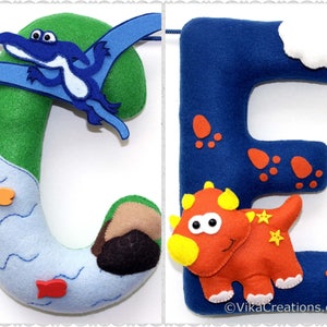 K&ouml;nnte beinhalten: Filzbuchstabenbanner mit den Buchstaben C und E. Der Buchstabe C ist gr&uuml;n mit einem blauen Pterodactylus und einem blauen Fluss mit orangefarbenen Fischen. Der Buchstabe E ist blau mit einem roten Dinosaurier und roten Dinosaurierspuren.