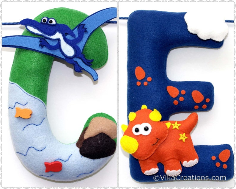 K&ouml;nnte beinhalten: Filzbuchstabenbanner mit den Buchstaben C und E. Der Buchstabe C ist gr&uuml;n mit einem blauen Pterodactylus und einem blauen Fluss mit orangefarbenen Fischen. Der Buchstabe E ist blau mit einem roten Dinosaurier und roten Dinosaurierspuren.