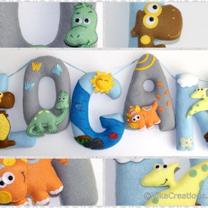 K&ouml;nnte beinhalten: Ein Filzbanner mit dem Namen "LOGAN" in grauen Buchstaben. Jeder Buchstabe ist mit einem anderen Dinosaurier und anderen Details wie einer Sonne, einer Wolke und einem Vulkan verziert.