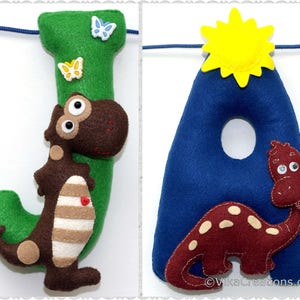 K&ouml;nnte beinhalten: Ein Filzbuchstabenbanner mit den Buchstaben J und A. Der Buchstabe J ist gr&uuml;n mit einem braunen Dinosaurier mit wei&szlig;en Streifen und einem roten Herzen auf dem Bauch. Der Buchstabe A ist blau mit einem roten Dinosaurier mit wei&szlig;en Flecken. Eine gelbe Sonne befindet sich &uuml;ber dem Buchstaben A.