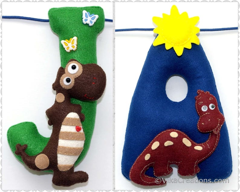 K&ouml;nnte beinhalten: Ein Filzbuchstabenbanner mit den Buchstaben J und A. Der Buchstabe J ist gr&uuml;n mit einem braunen Dinosaurier mit wei&szlig;en Streifen und einem roten Herzen auf dem Bauch. Der Buchstabe A ist blau mit einem roten Dinosaurier mit wei&szlig;en Flecken. Eine gelbe Sonne befindet sich &uuml;ber dem Buchstaben A.