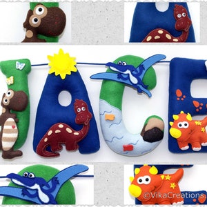 K&ouml;nnte beinhalten: Ein Filzbanner mit dem Namen "Jace" in gro&szlig;en blauen Buchstaben. Jeder Buchstabe ist mit einem anderen Dinosaurier und anderen Details wie einer Sonne, einem Berg und einem Fluss verziert. Das Banner ist perfekt f&uuml;r ein Kinderzimmer.