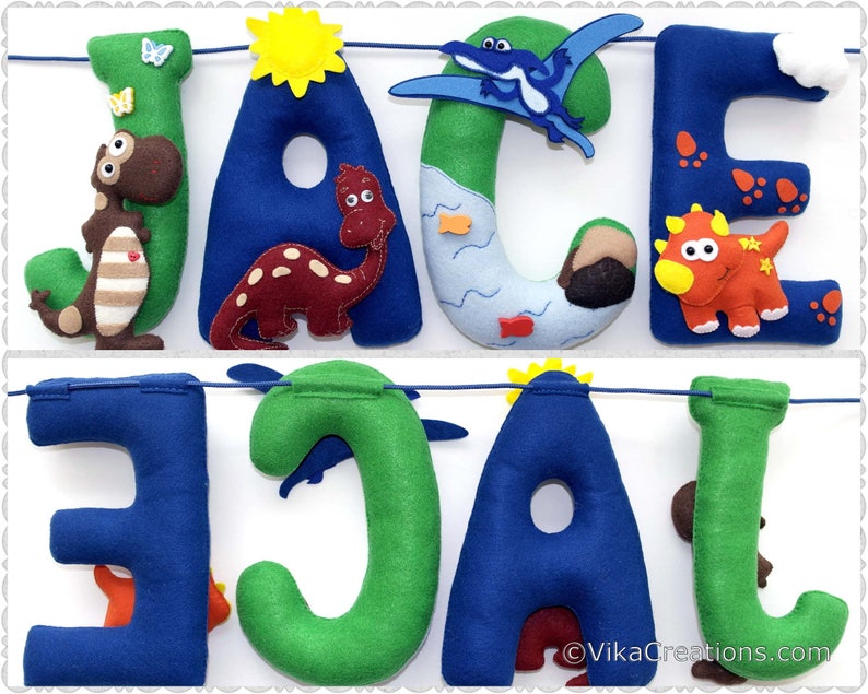 K&ouml;nnte beinhalten: Ein Filzbanner mit dem Namen "JACE" in blauen und gr&uuml;nen Buchstaben. Jeder Buchstabe ist mit einem anderen Dinosaurier-Charakter verziert, darunter ein Pterodactylus, ein Stegosaurus, ein Triceratops und ein Tyrannosaurus Rex. Das Banner ist mit einer blauen Schnur befestigt und hat einen wei&szlig;en Hintergrund.