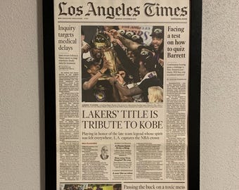 May include: A front page newspaper article from the Los Angeles Times, dated October 12, 2020, with the headline "LAKERS' TITLE IS TRIBUTE TO KOBE". The article features a photo of the Los Angeles Lakers basketball team celebrating their NBA championship victory. The article also includes a photo of a woman in a black mask and a woman in a white shirt, and a photo of a man in a white shirt and blue shorts playing tennis.