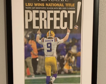 May include: Framed newspaper front page with the headline "LSU WINS NATIONAL TITLE" and the word "PERFECT!" in large letters. The image features a football player in a yellow and purple uniform. The frame is black.