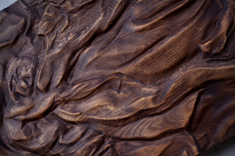 May include: Close-up of a dark brown, carved wooden panel. The wood grain is visible, with a textured, undulating surface. The carving has a flowing, organic design, with deep grooves and ridges. The overall effect is rustic and artistic.