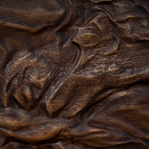 May include: Close-up of a richly textured, dark brown wooden surface. The wood grain is visible, with a pattern of flowing, organic shapes and deep grooves. The surface has a natural, aged appearance.