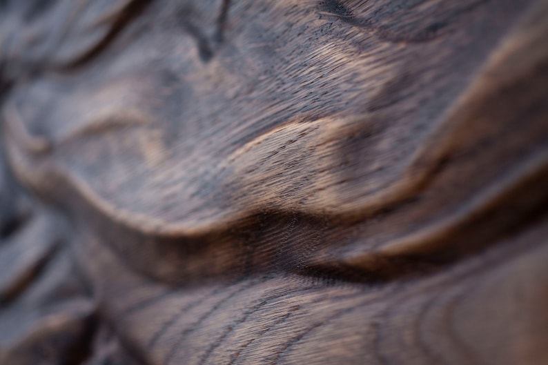May include: Close-up of a dark brown wooden surface with a wavy, textured pattern. The wood grain is visible, with lighter brown highlights contrasting against the darker tones. The image focuses on the natural texture and color variations.
