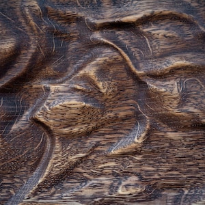 May include: Close-up of a textured wooden surface with a dark brown color. The wood grain has a wavy pattern, creating a natural, organic look. The surface appears to be carved or sculpted.