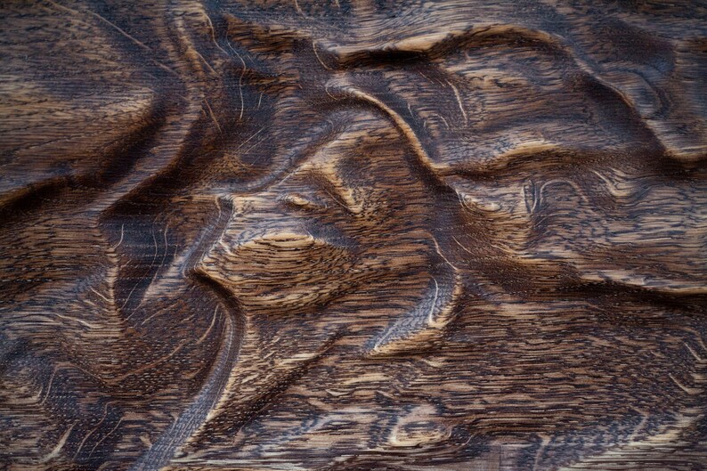 May include: Close-up of a textured wooden surface with a dark brown color. The wood grain has a wavy pattern, creating a natural, organic look. The surface appears to be carved or sculpted.