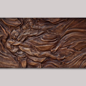 May include: A rectangular, wooden wall art piece with a carved, flowing design. The artwork features a rich, dark brown color with visible wood grain, creating a textured and organic appearance. The carved patterns resemble waves or fabric folds.