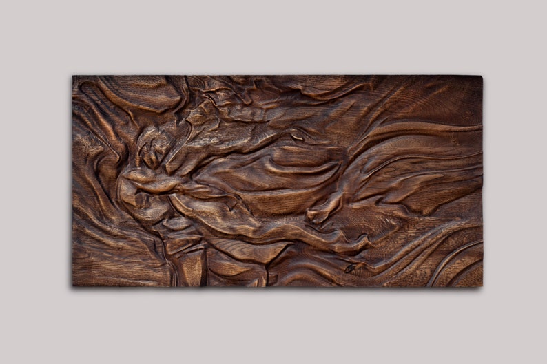 May include: A rectangular, wooden wall art piece with a carved, flowing design. The artwork features a rich, dark brown color with visible wood grain, creating a textured and organic appearance. The carved patterns resemble waves or fabric folds.